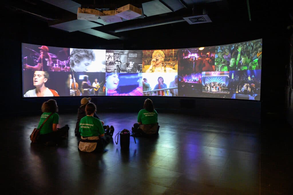 Tour participants sitting in a dark theatre looking at screens of country music stars