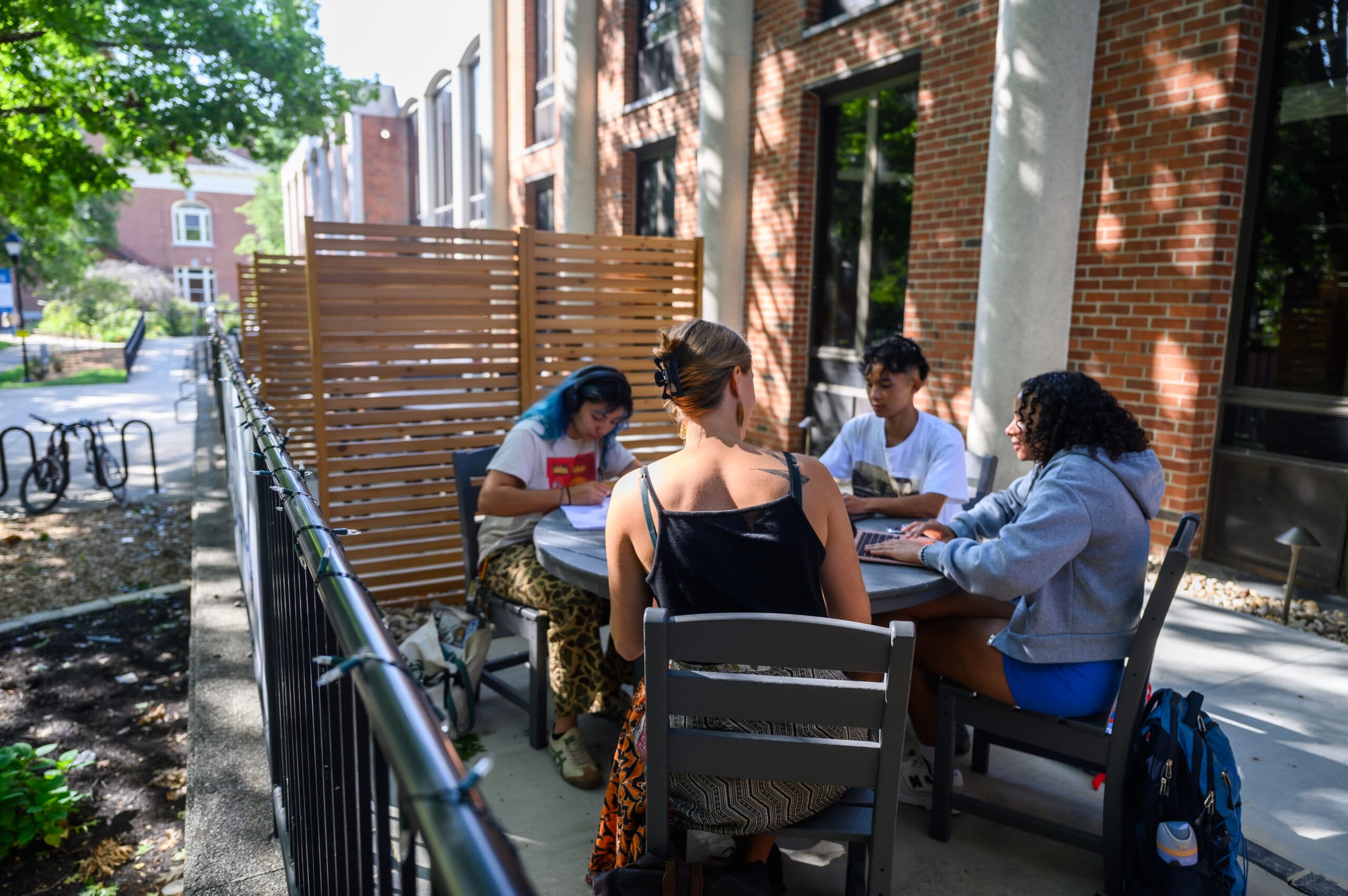 Several students are sitting at an outdoor table, engaged in studying.