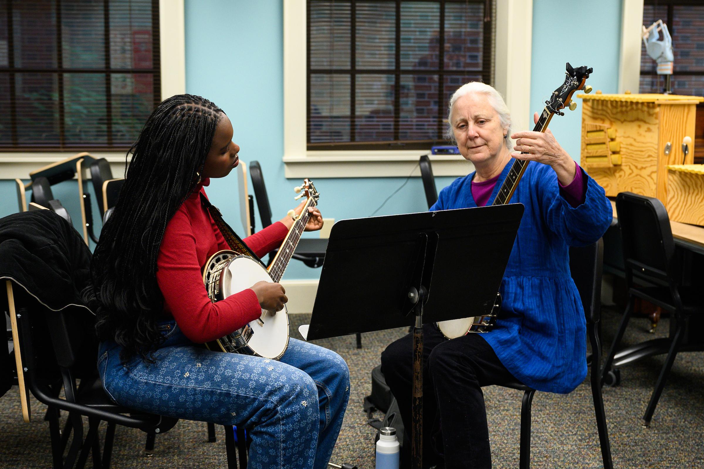 Two women play banjo beside one another during a practice session.