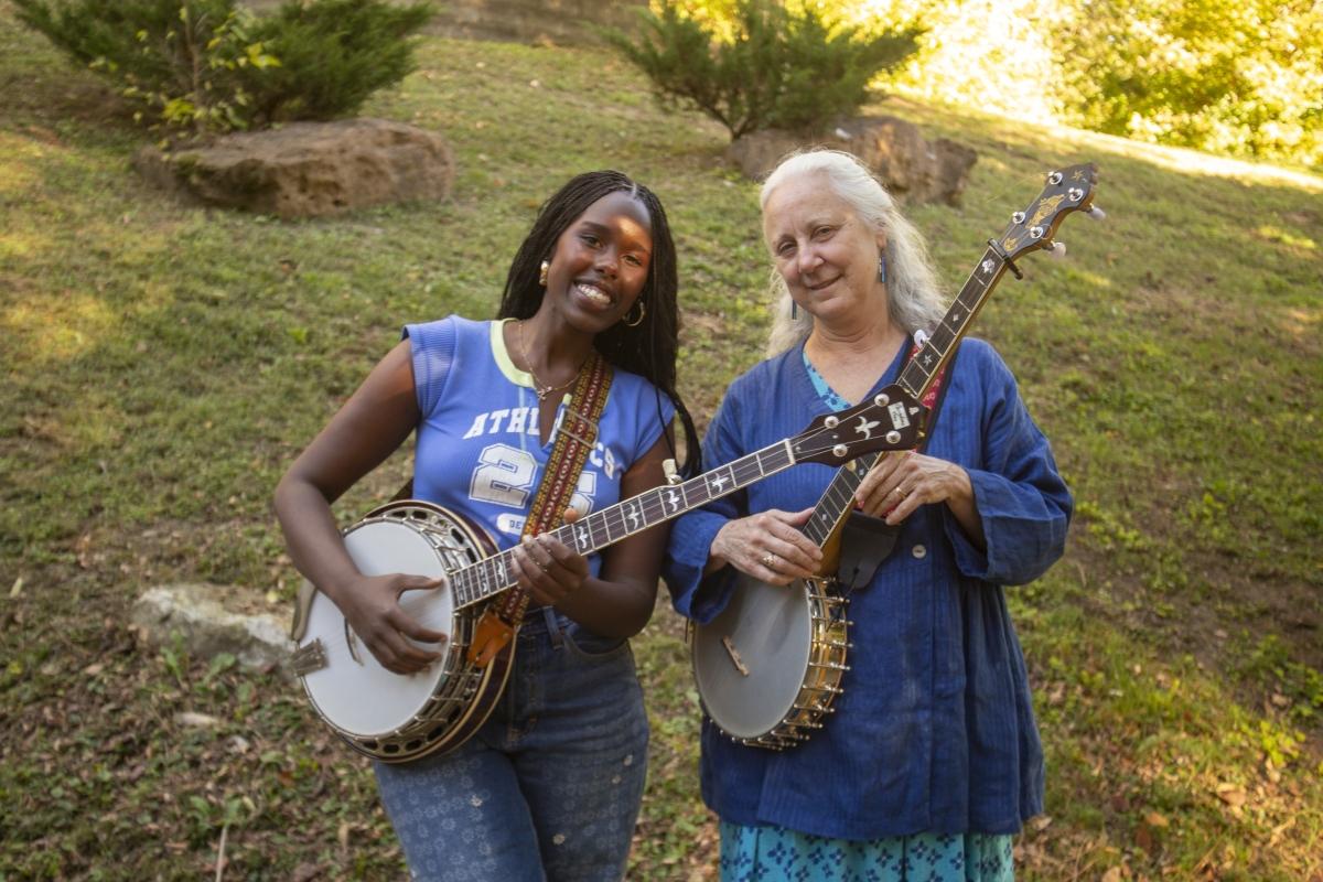 Two smiling women standing beside one another, each holding their own banjo.